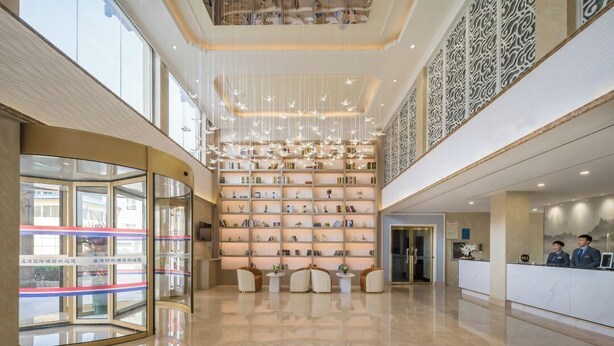 Een ruime lobby met een centrale boekenkast, een receptiebalie en een glazen ingang.