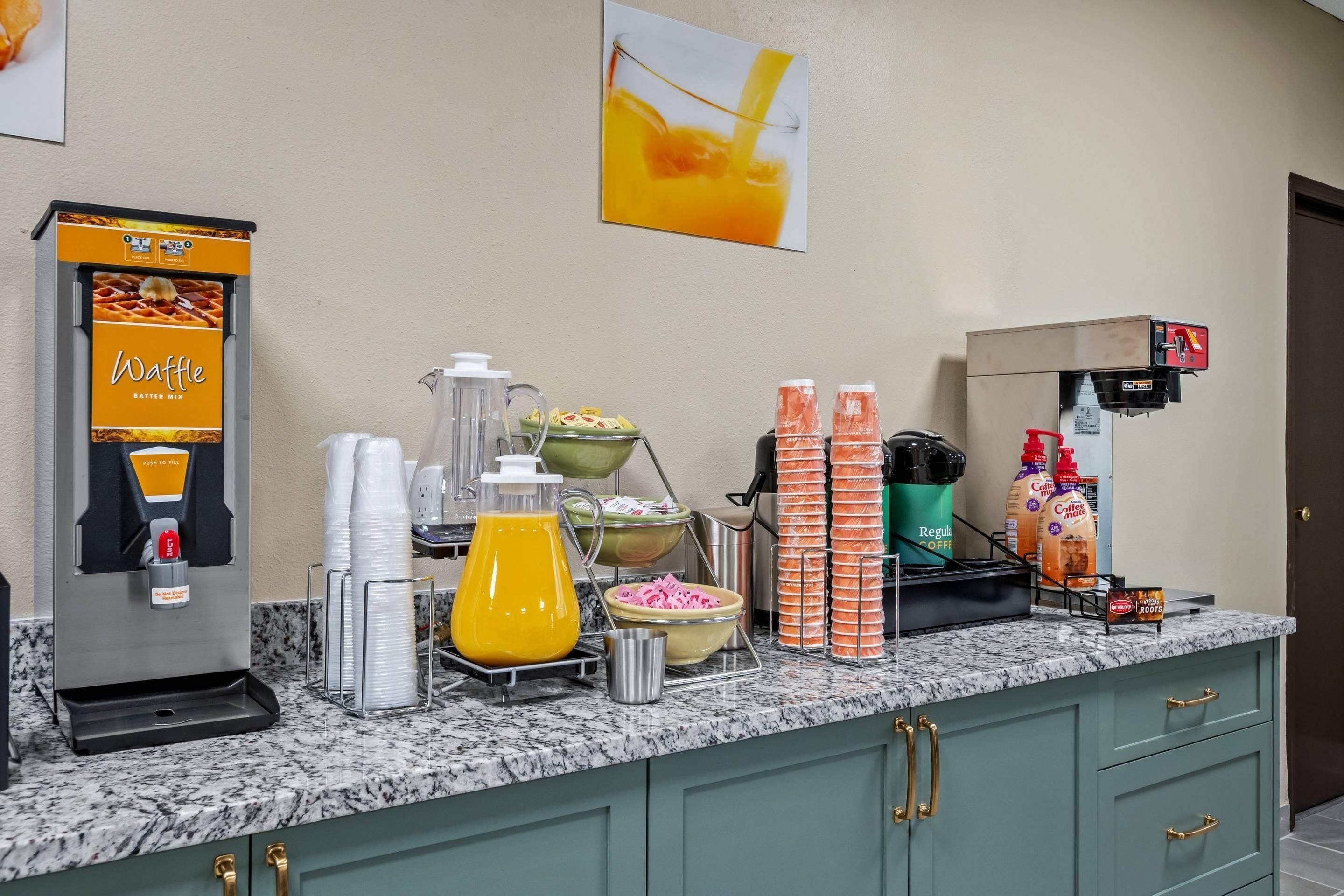 A breakfast bar with a waffle maker, coffee machine, and various food items.