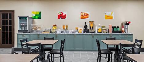 A cafeteria with multiple tables and chairs, a coffee machine, and various food items on display.