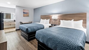 Habitación de hotel con dos camas, un escritorio, una silla, un baño y un cuadro en la pared.