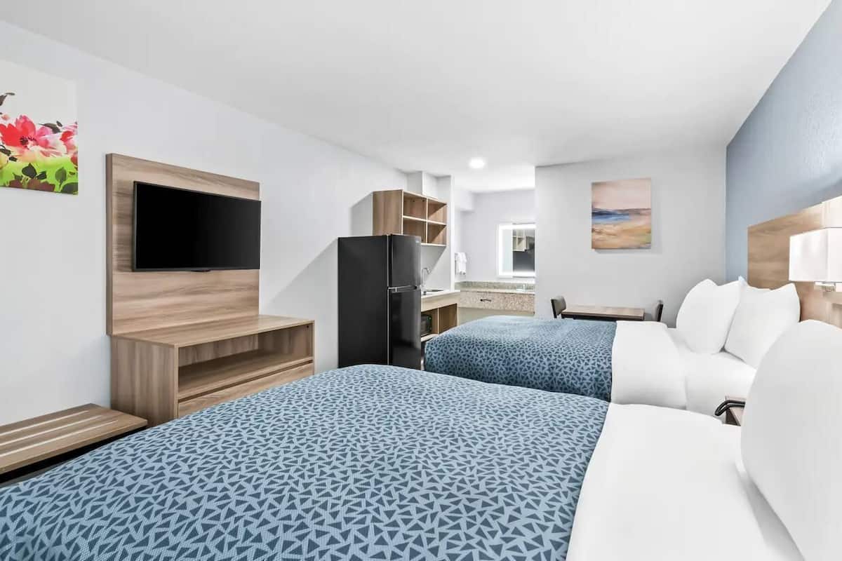 A hotel room with two beds, a TV, a refrigerator, a desk, and a window.