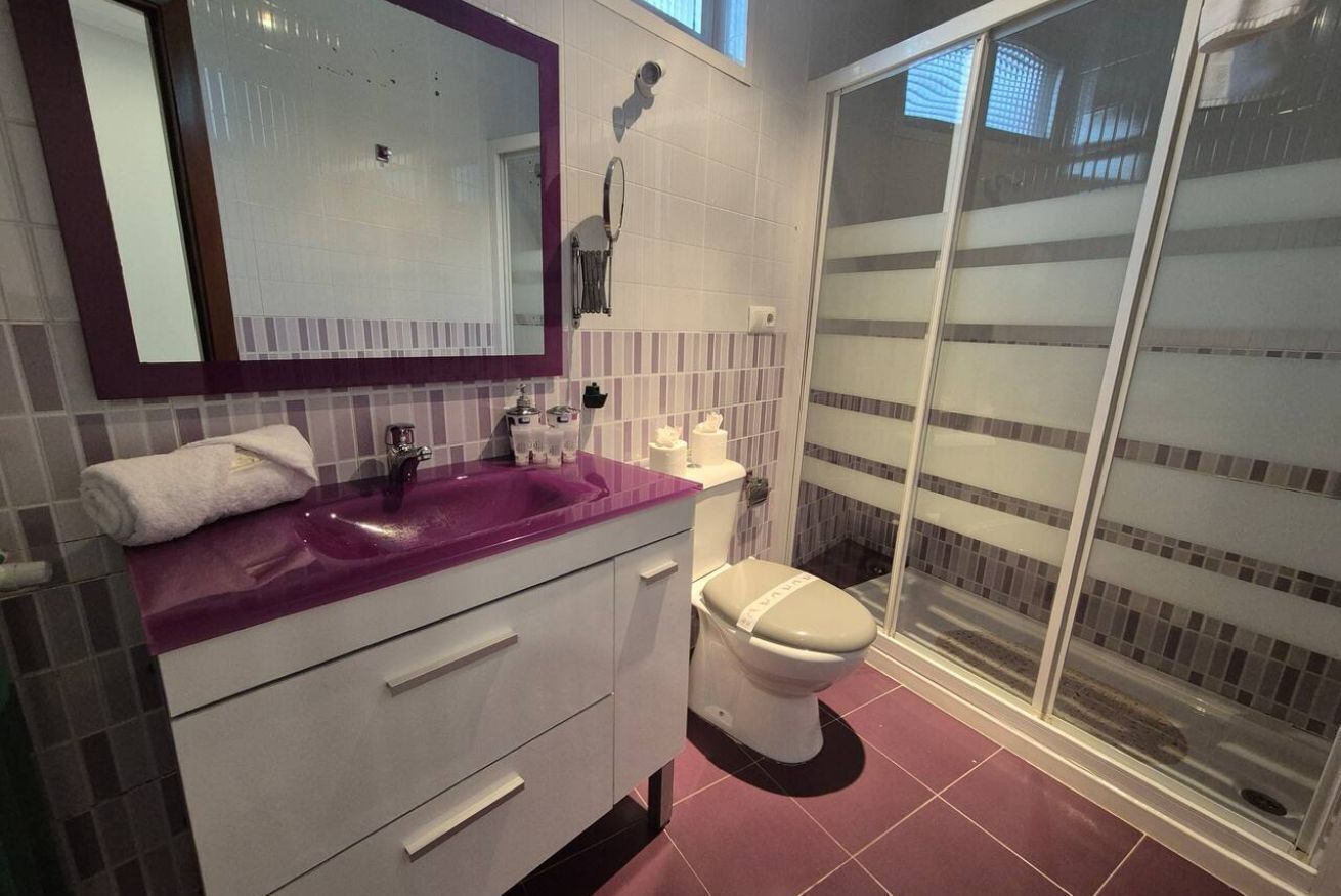 Un baño con lavamanos morado, inodoro blanco y cabina de ducha de vidrio.