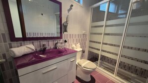 A bathroom with a purple sink, white toilet, and a glass shower enclosure.