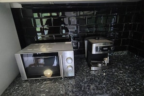 Een keuken met een magnetron, een koffiezetapparaat en een zwart betegelde spatwand.