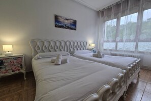 A double bed with a unique headboard, a bedside table with a lamp, and a window with a view.