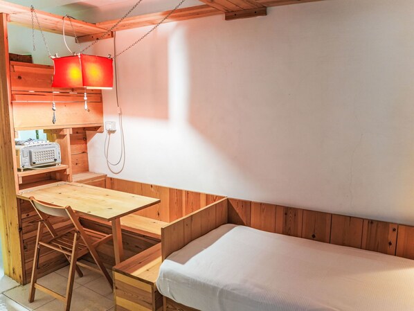 A compact room with a wooden desk, a chair, a bed, and a red hanging light fixture.