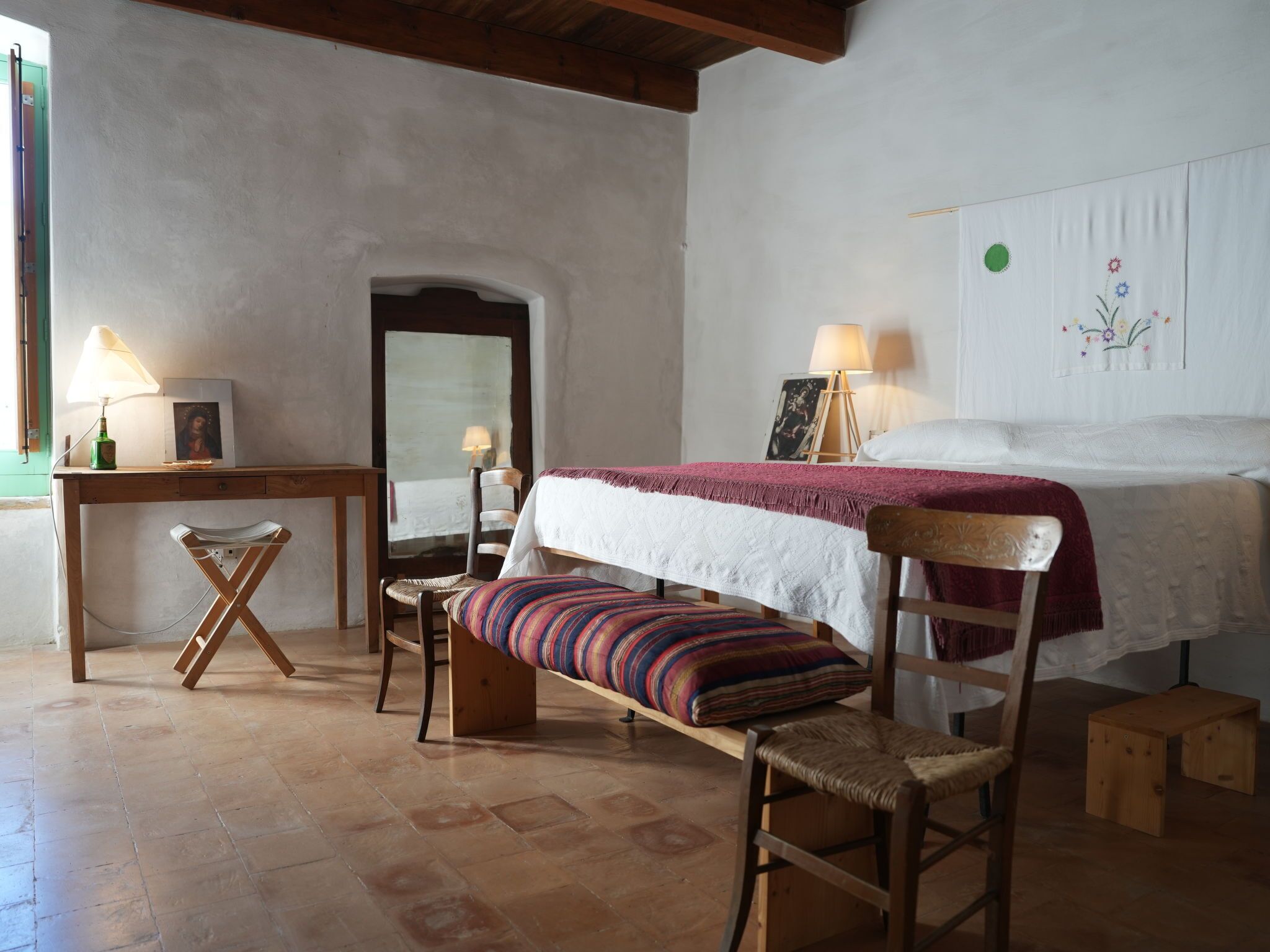 Un dormitorio con una cama, un banco, una silla, una mesita y un espejo.