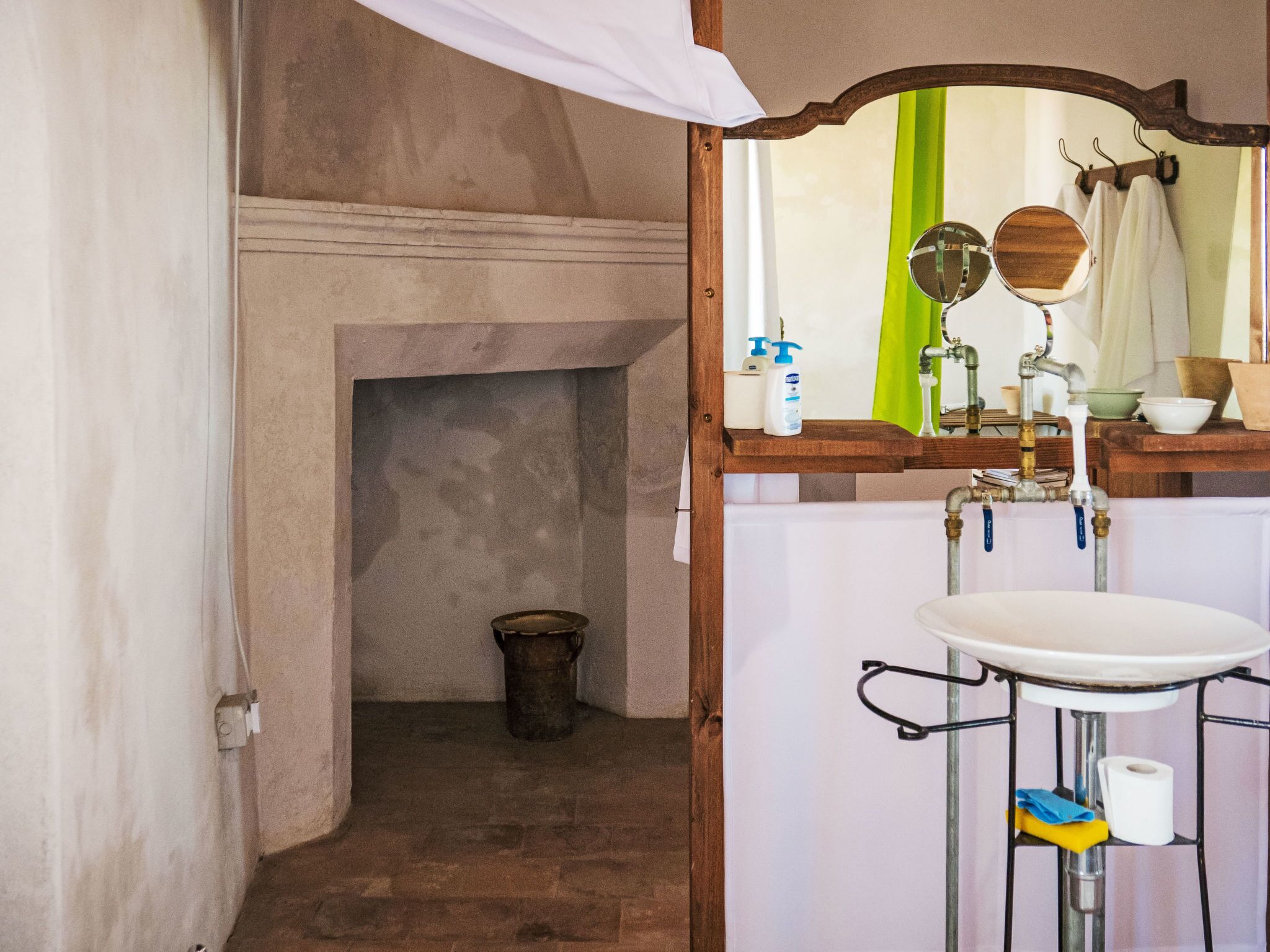 A bathroom with a wooden vanity, a mirror, a sink, and a bucket on the floor.