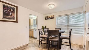 Un comedor con una mesa redonda y cuatro sillas, una cocina al fondo y una ventana con persianas.