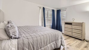 Un dormitorio con cama, cómoda y ventana con cortinas.