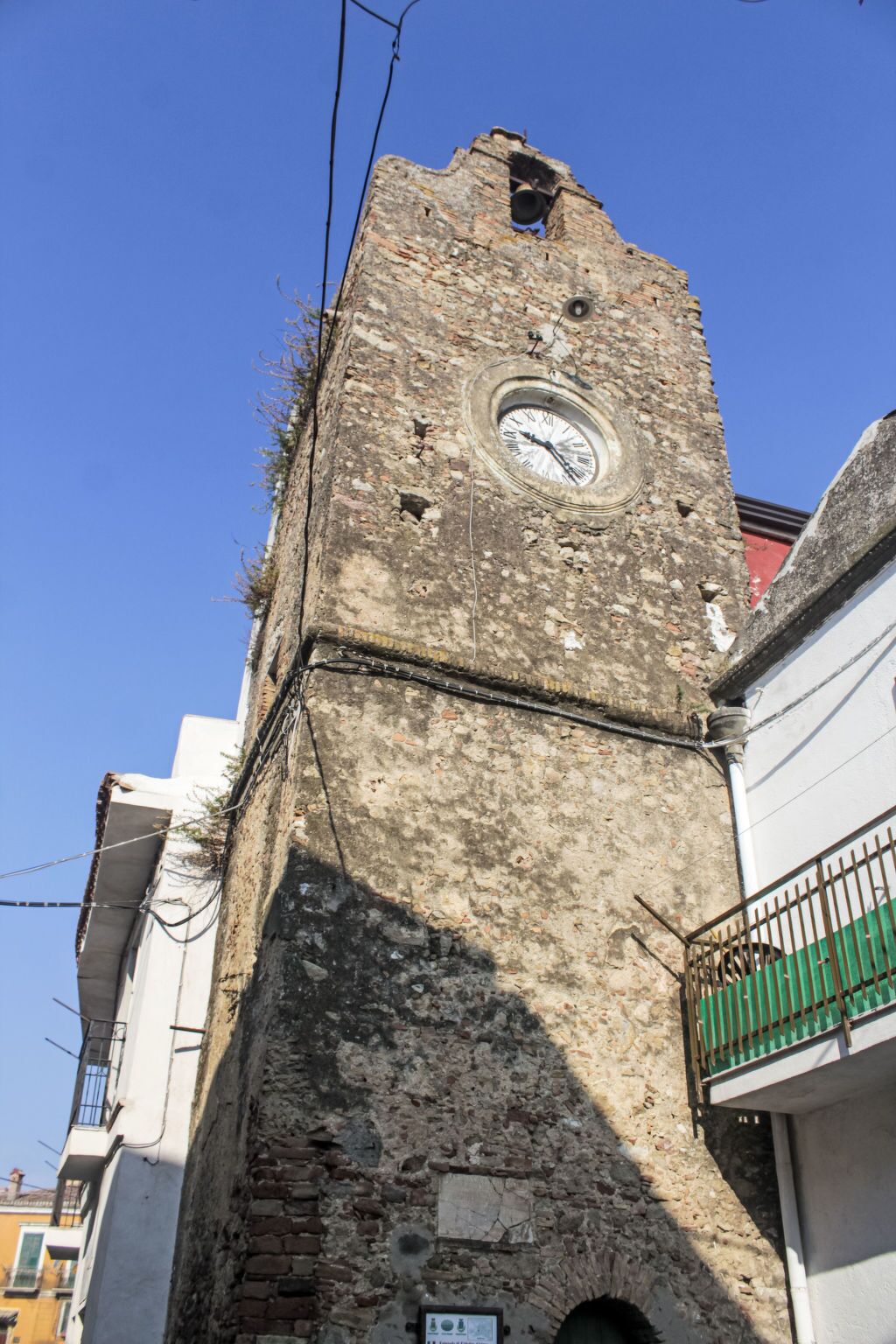 Una alta torre de piedra histórica con una esfera horaria, rodeada de edificios modernos.