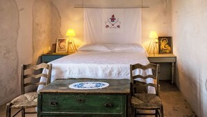 Habitació tradicional amb un llit, dues taules de nit, un taulell verd, dues cadires de vimetla i un tapís mural.