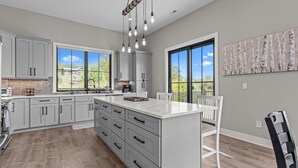 Une cuisine moderne avec des meubles gris, un grand îlot central et des luminaires suspendus.