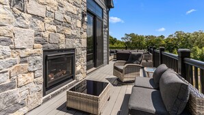 Un mur extérieur en pierre avec une cheminée, du mobilier d’extérieur et une terrasse en bois.