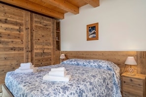 A bedroom with a wooden headboard, a bed with a floral bedspread, a nightstand with a lamp, and a framed picture on the wall.