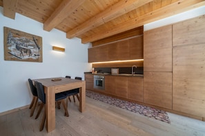 A modern kitchen with wooden cabinets, a dining table with chairs, and a painting on the wall.