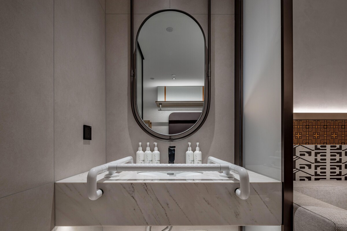 A modern bathroom with a marble sink, a large mirror, and a wall-mounted towel dispenser.