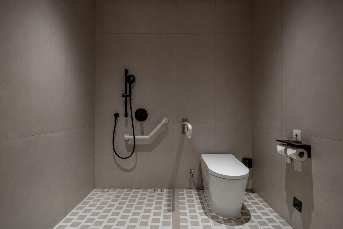 A modern bathroom with a toilet, shower, and handrails.