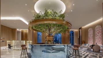 A modern lobby with a central circular bar, a large tree, and a seating area with bar stools.