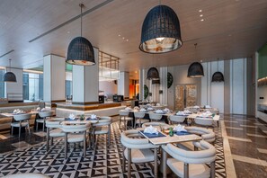 A modern dining area with round tables and chairs, pendant lighting, and a geometric patterned floor. - Even Yining By Ihg (Yining)