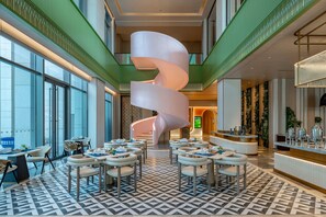 Un moderno vestíbulo de hotel con una escalera espiral, zonas de estar y una recepción.