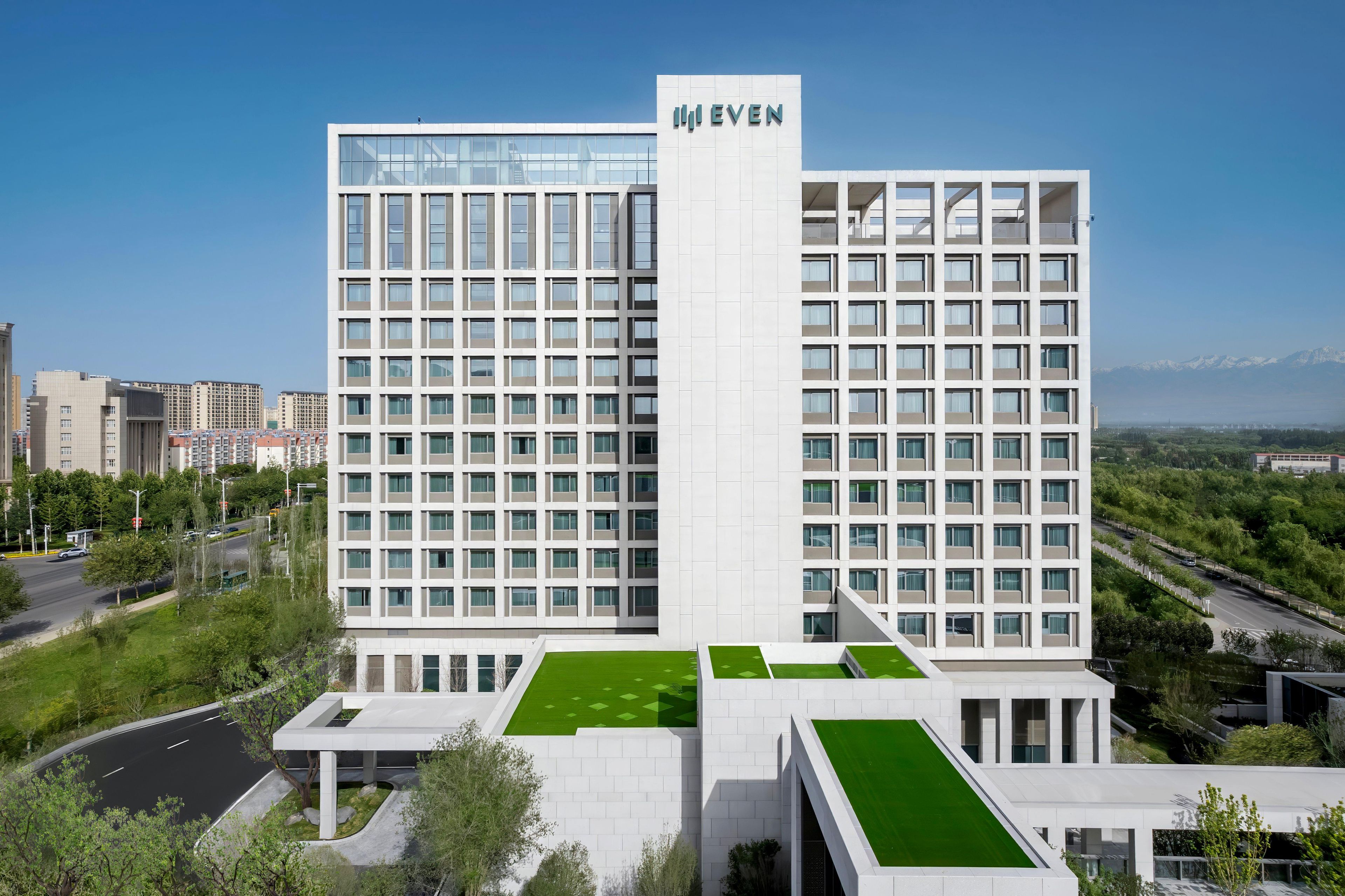 A modern hotel with a prominent 'EVEN' sign, featuring a grid of windows and a flat roof with green areas.