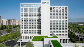 A modern hotel with a prominent 'EVEN' sign, featuring a grid of windows and a flat roof with green areas.
