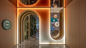 A modern interior with a reception desk, a curved wall with a reflective surface, and a hallway leading to another area.