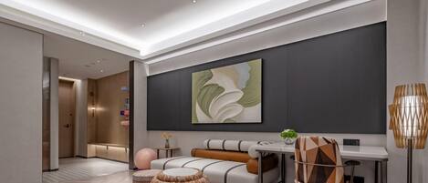A modern hotel room with a sofa, ottoman, desk, and chair.