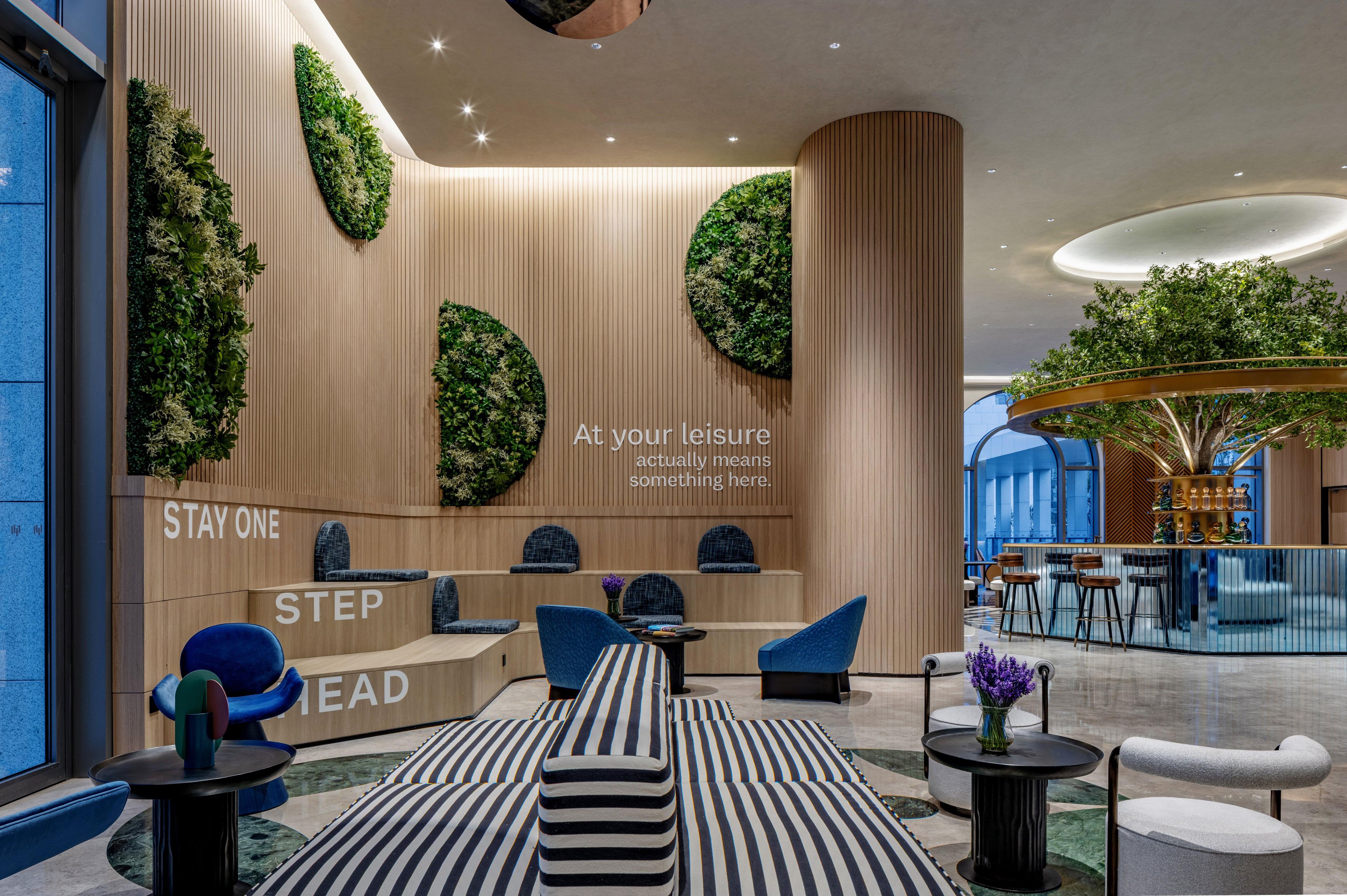 A modern hotel lobby with a reception desk, seating area, and a large indoor garden.