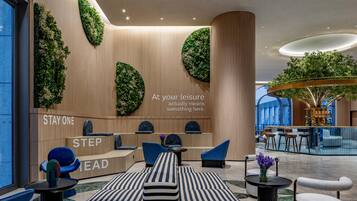 A modern hotel lobby with a reception desk, seating area, and a large indoor garden.