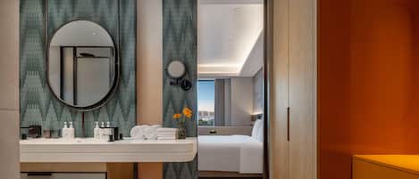A modern hotel room with a bathroom, a bed, and a view of the city.