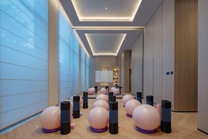 Un interior de hotel moderno con pelotas de ejercicio y pesas, un largo pasillo y una recepción a lo lejos.