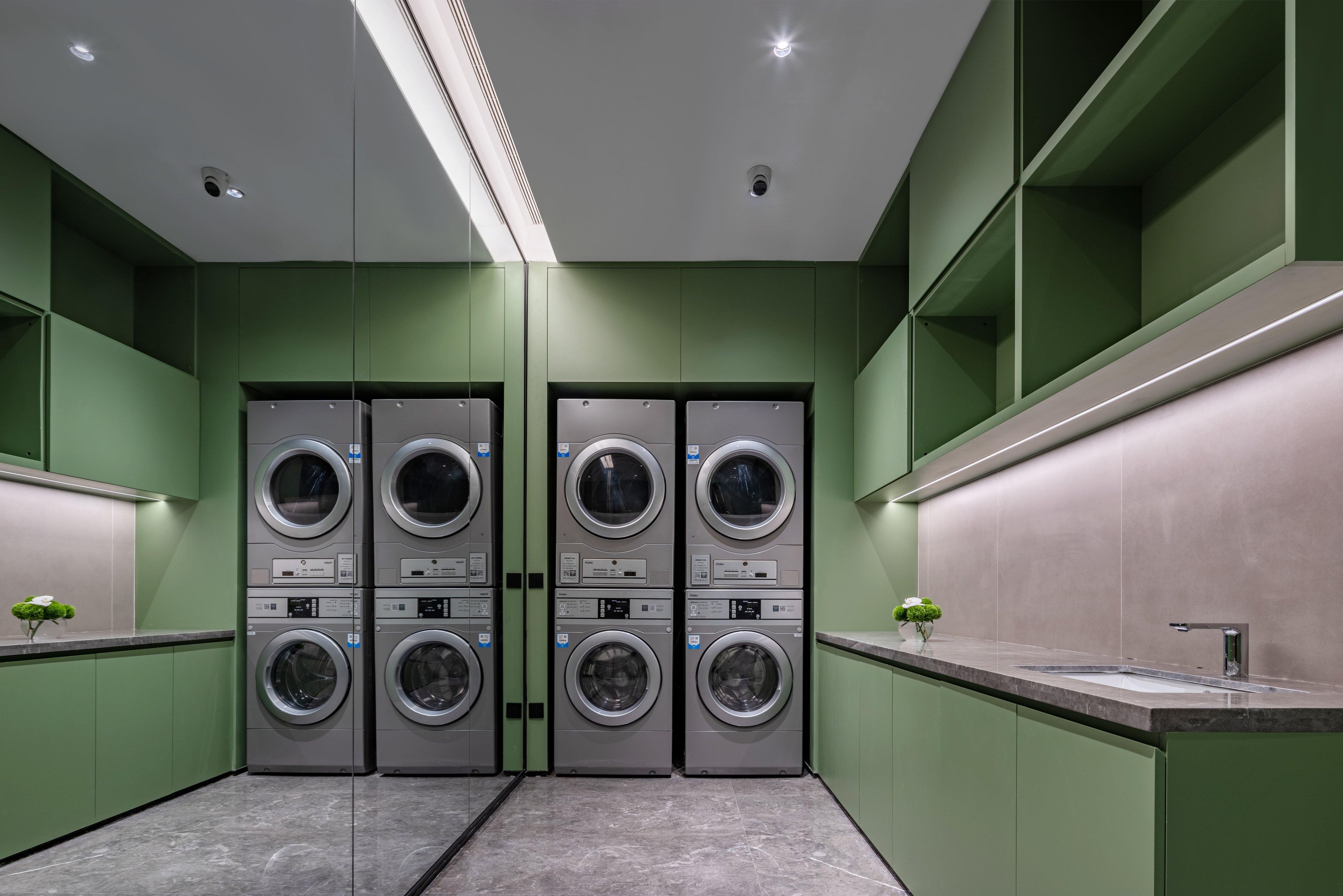 A modern laundry facility with four stacked washing machines, a sink, and green walls.