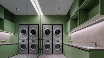 A modern laundry facility with four stacked washing machines, a sink, and green walls.