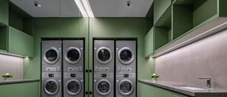 A modern laundry facility with four stacked washing machines, a sink, and green walls.