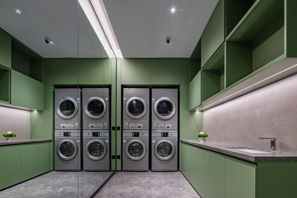 A modern laundry facility with four stacked washing machines, a sink, and green walls.