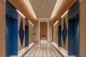 Un couloir d’hôtel moderne avec un sol à motifs géométriques, des panneaux de bois sur les murs et une composition florale décorative au centre.