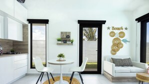 Une cuisine moderne avec des meubles blancs, un coin repas doté d’une table ronde et de chaises, et un salon avec un canapé blanc et des œuvres d’art décoratives au mur.