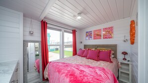 A bedroom with a large bed, a window with red curtains, and a view of a tennis court. - The Boozy Bungalow at Roadrunner Resort (Parker)