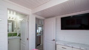 A bedroom with a bed, a television, a bathroom with a mirror and sink, and a kitchen area. - The Boozy Bungalow at Roadrunner Resort (Parker)
