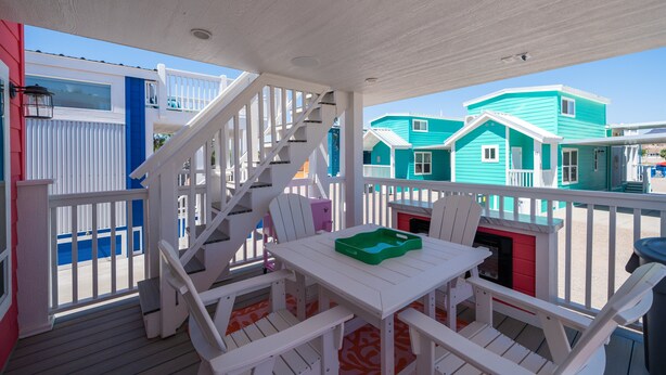 A covered outdoor deck with white railings, a table, and chairs. - The Boozy Bungalow at Roadrunner Resort (Parker)