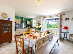 A kitchen with wooden cabinets, a dining table set with chairs, and a view of the outdoors. - L'Horizon by Interhome (La Bernerie-en Retz)