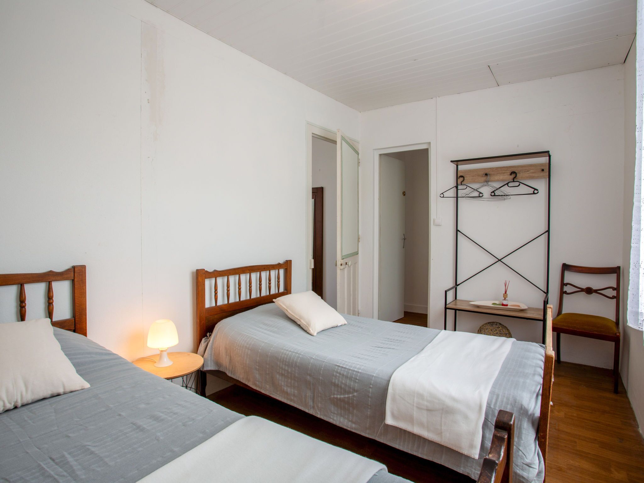 A bedroom with two beds, a wooden headboard, a bedside table with a lamp, and a clothing rack.