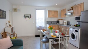 Une cuisine moderne avec des meubles blancs, une table à manger avec des chaises, un lave-linge et un petit coin repas comprenant un canapé et un fauteuil.
