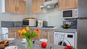 Une cuisine moderne avec des meubles en bois, un four à micro-ondes, une machine à café et un lave-vaisselle. Il y a des tulipes sur la table et un saladier rempli de fraises.