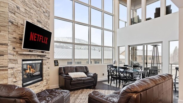 A living room with a stone wall, a fireplace, a leather sofa, a TV mounted on the wall, and large windows. - 3min Walk to Ski Lifts*Movie Theater*Views (Brian Head)