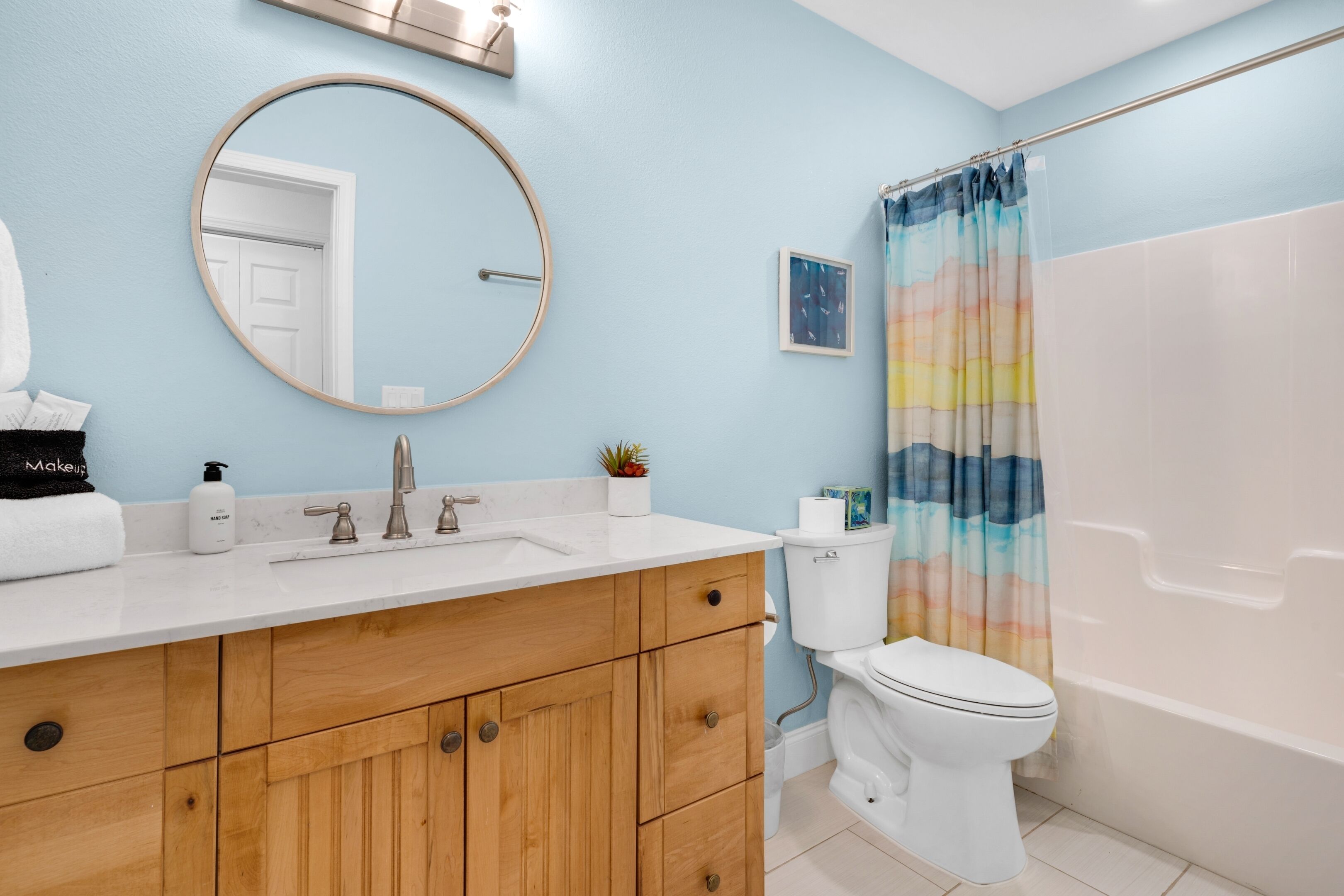 Een badkamer met een houten wastafelmeubel, een ronde spiegel, een toilet en een douchegordijn.