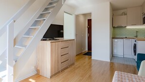 A modern kitchen with a built-in dishwasher and washing machine, a wooden dining table, and a staircase leading to an upper level.