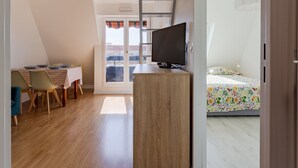 A bedroom with a bed, a TV, a desk with chairs, and a balcony with a view.